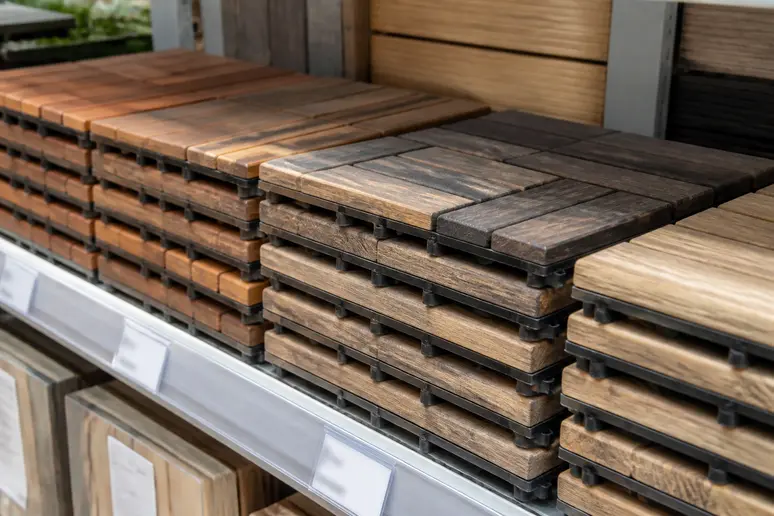 Plusieurs types de caillebotis en bois exotique sont présentés en magasin, avec des étiquettes de prix suggérant leur coût variable.