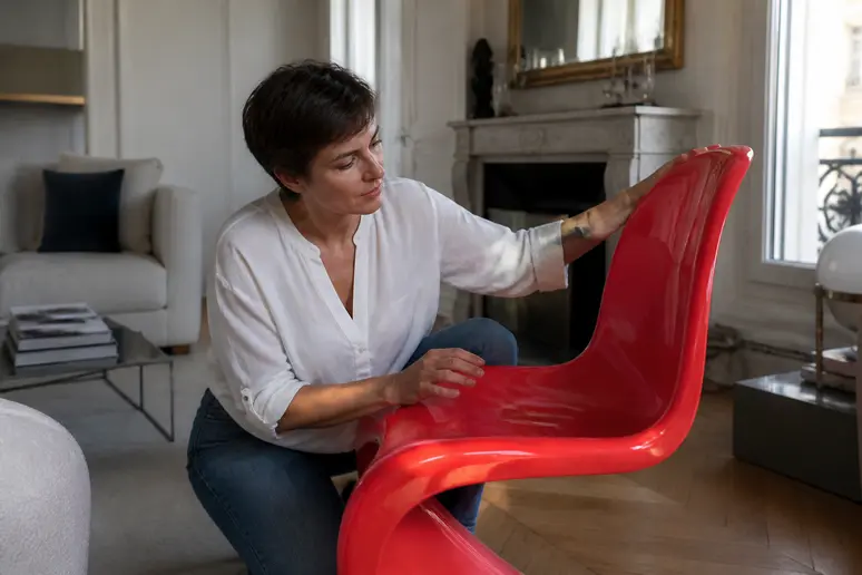 Une femme parisienne examine attentivement la texture d'une chaise Panton rouge dans son salon lumineux.