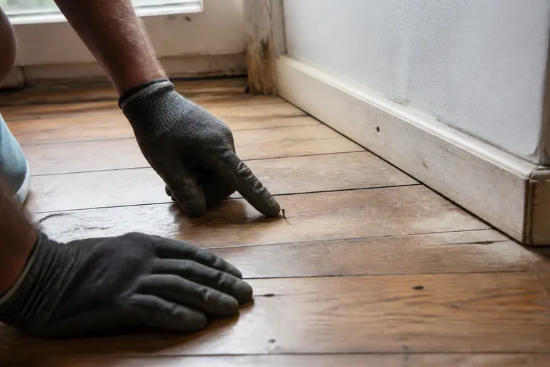 Des mains gantées vérifient méticuleusement un parquet pour préparer le ponçage, assurant la sécurité et le ponçage-parquet.