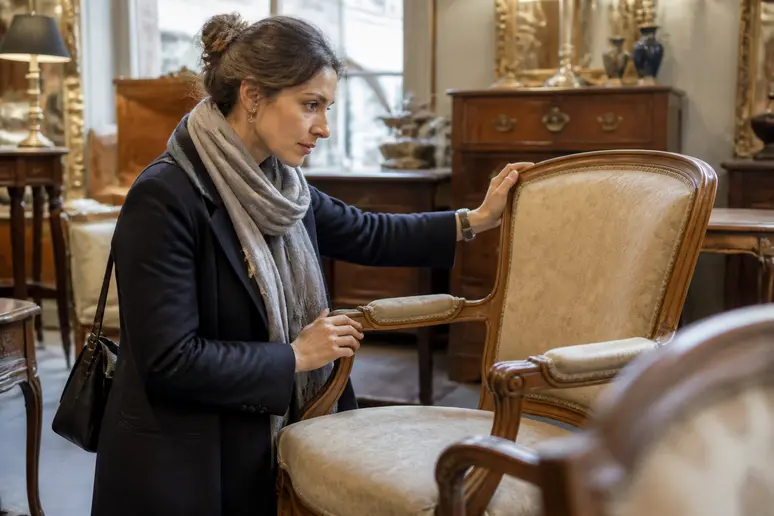 Une femme cherche une chaise vintage dans un magasin d'antiquités, un achat potentiel sur Selency.