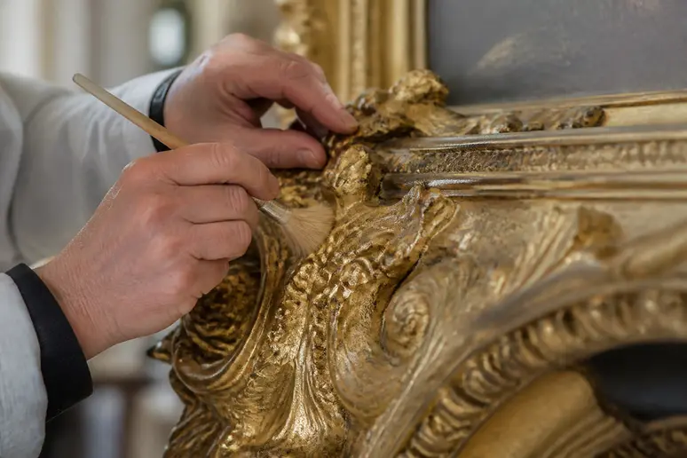 Gros plan sur la dorure authentique d'un cadre baroque ancien lors d'une restauration.