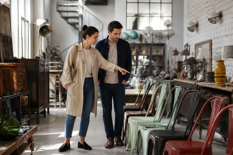 Un couple choisit une chaise Tolix vintage authentique dans une boutique, considérant leur prix.
