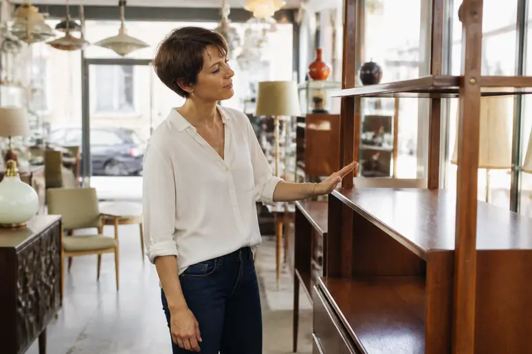 Une femme examine attentivement une étagère vintage en bois dans une brocante parisienne.
