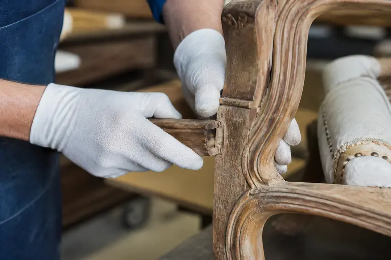 Mains d'un restaurateur ajustant un assemblage tenon-mortise sur un fauteuil Louis XV authentique.