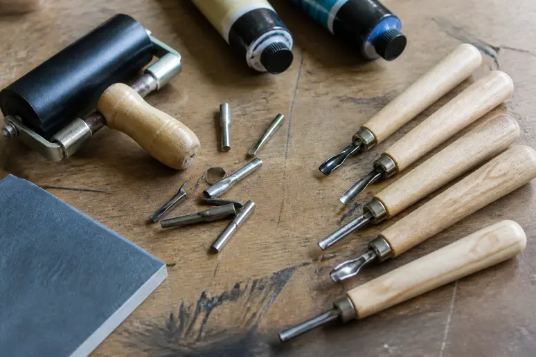 Collection d'outils de linogravure sur un établi en bois, prêts à l'emploi.