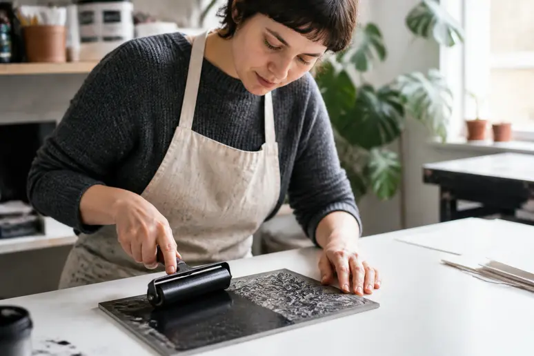 Mains d'une artiste en train d'encrer une plaque de linogravure avec un rouleau.