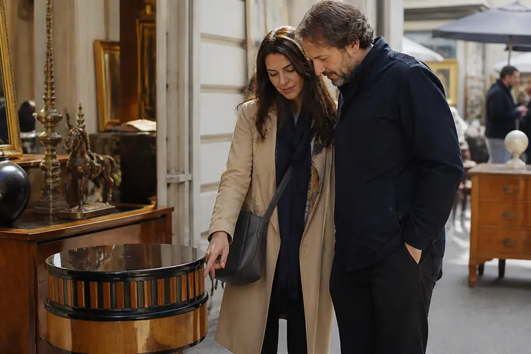 Un couple à Paris examine avec intérêt un meuble Art Déco, estimant la valeur d'un trésor d'époque.