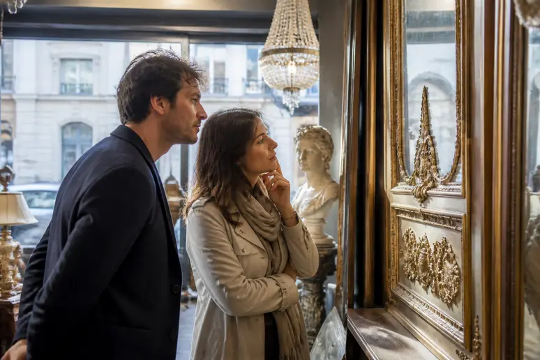 Couple admirant un trumeau ancien aux ornements sculptés dans une boutique parisienne.