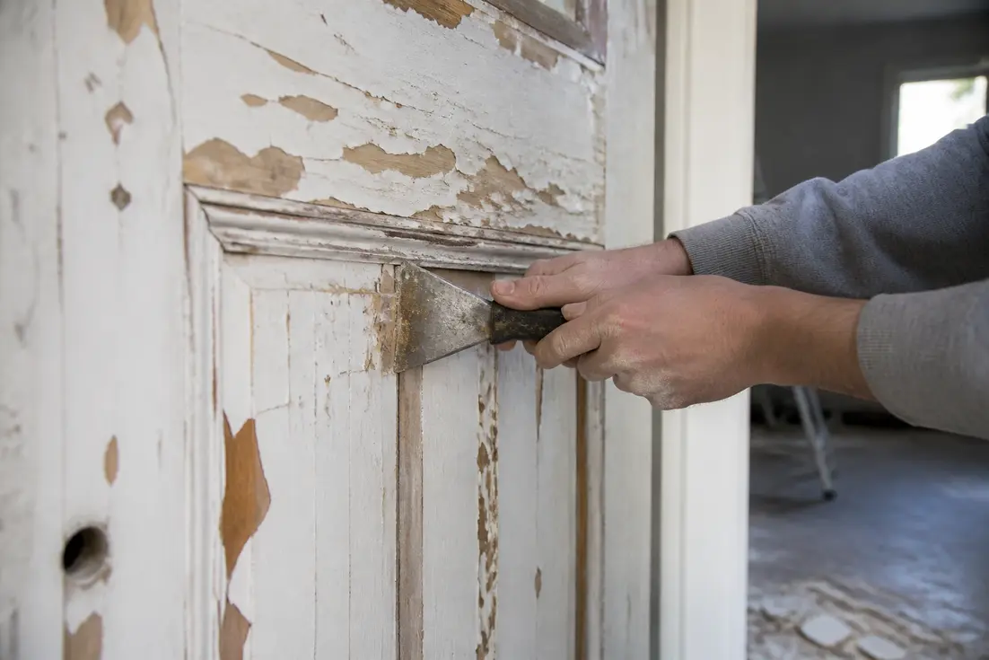 Artisan retirant la vieille peinture sur une porte en bois illustrant l ecaillage des surfaces