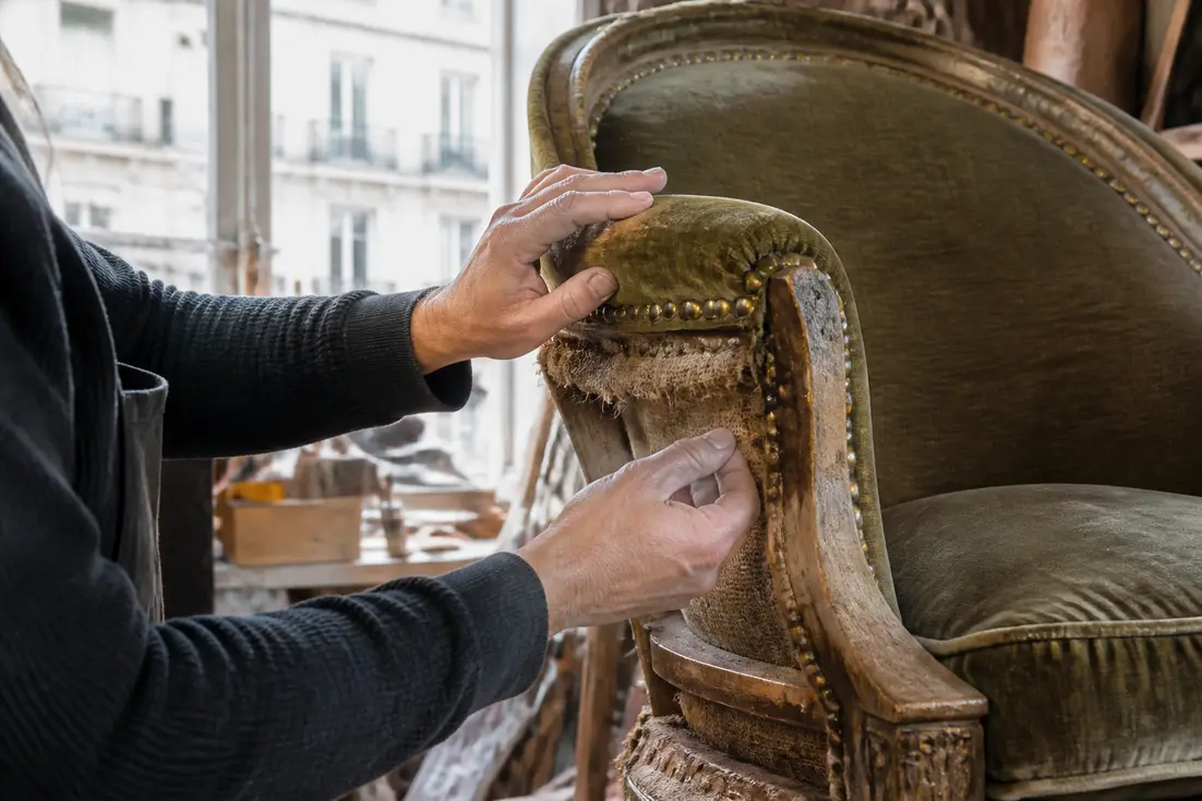 Un artisan examine les détails d'un fauteuil crapaud vintage dans son atelier lumineux.
