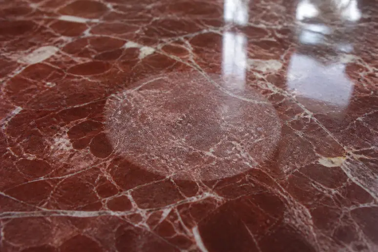 Zone mate sur un plateau en marbre rouge suite à une corrosion par un acide