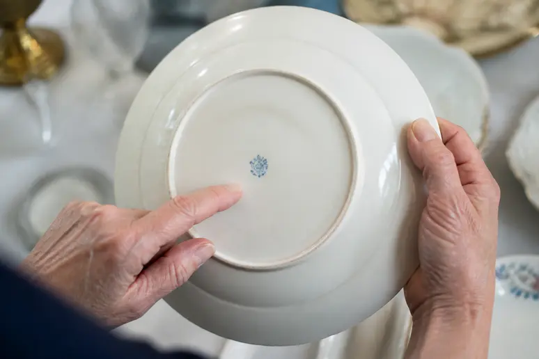 Mains inspectant la signature sous une assiette en porcelaine de Sologne ancienne