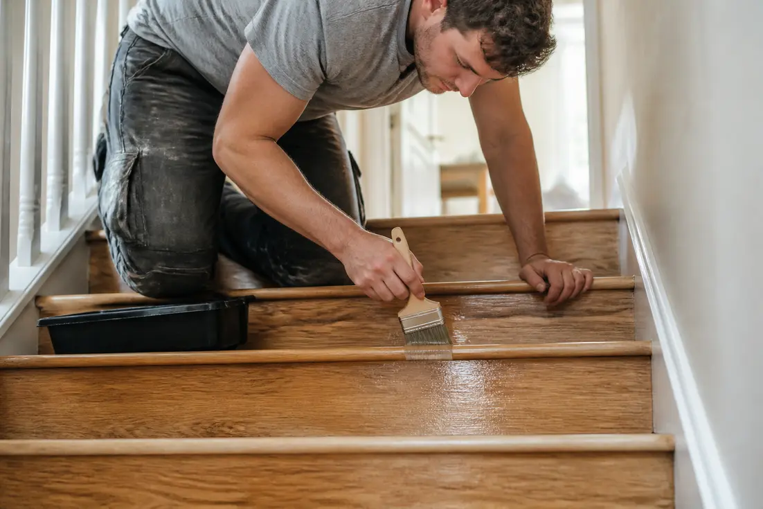Application d'un vitrificateur pour escalier au pinceau sur des marches en bois lors de travaux de rénovation