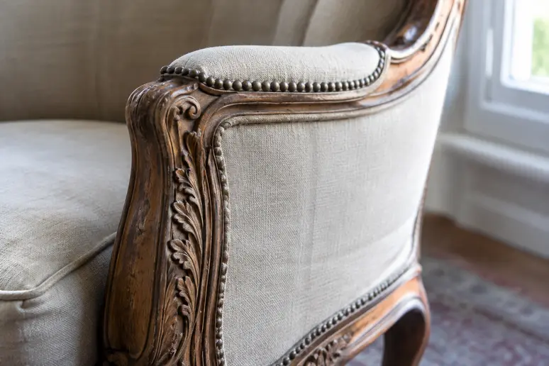 Gros plan sur les sculptures en bois et les courbes d'un fauteuil bergère ancien.