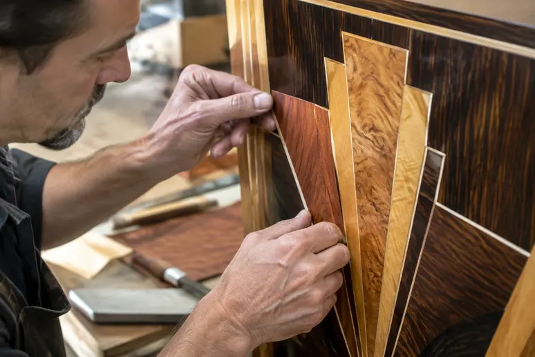 Artisan réalisant une marqueterie en bois précieux sur un meuble art deco haut de gamme